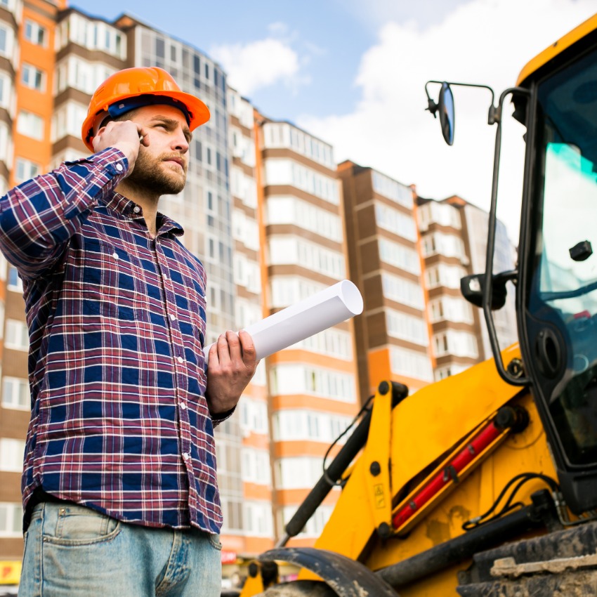 Un employé de chantier est au téléphone devant son tracteur jaune