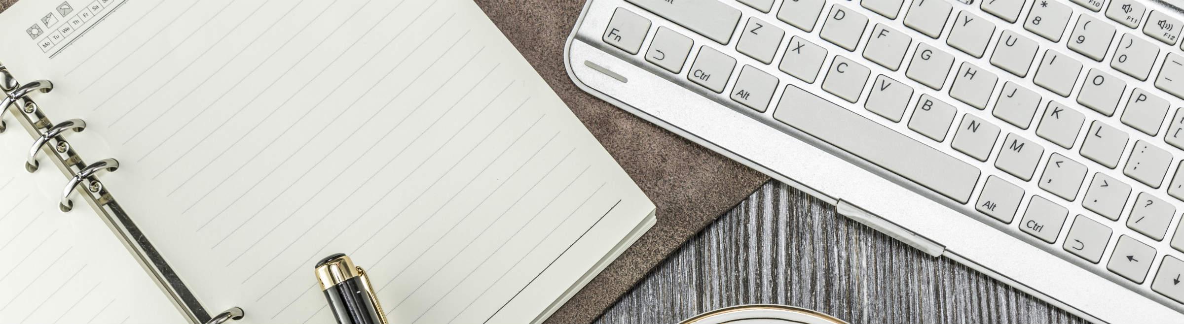 Un bureau avec un clavier d'ordinateur, un bloc-notes et un stylo