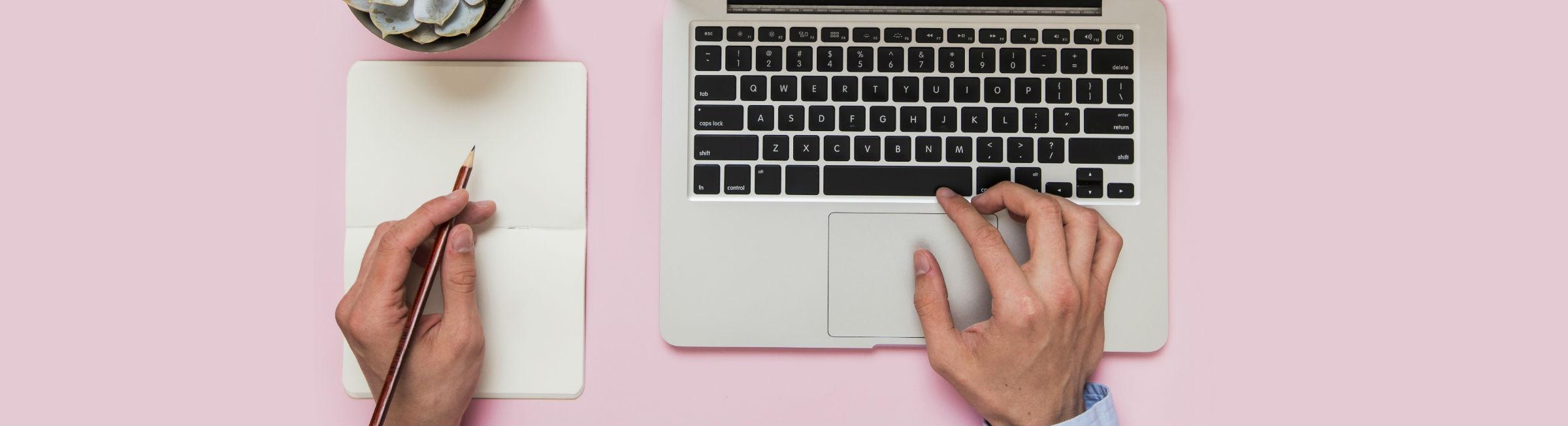 Une personne écrit de la main gauche sur un calepin et navigue sur son ordinateur portable avec sa main droite
